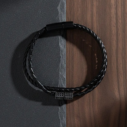 Black braided bracelet with a clasp on a dark gray and wooden surface