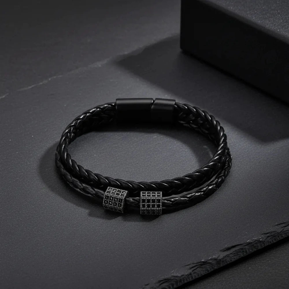 Black braided leather bracelet with metal clasp on a dark surface