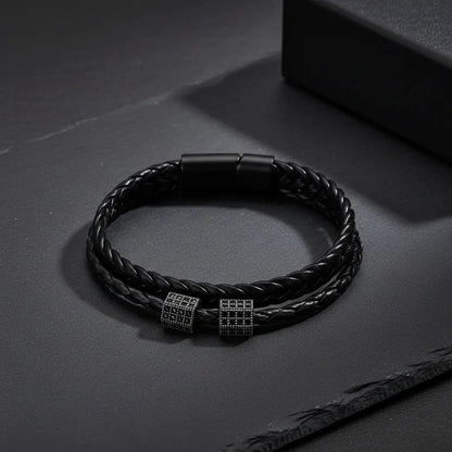 Black braided leather bracelet with metal clasp on a dark surface