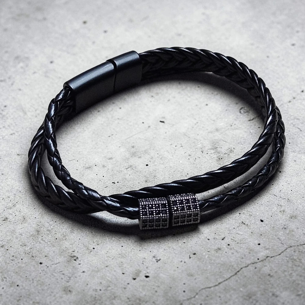 Black braided leather bracelet with a metallic clasp on a concrete surface