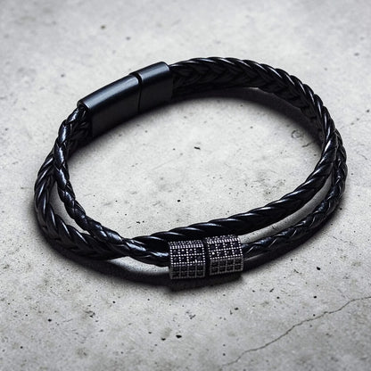 Black braided leather bracelet with a metallic clasp on a concrete surface