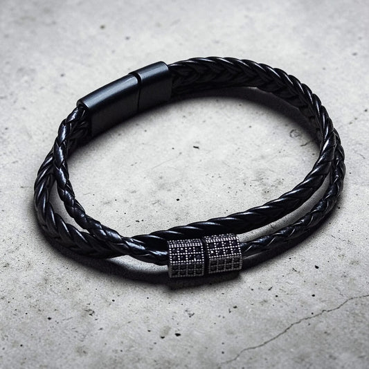 Black braided leather bracelet with a metallic clasp on a concrete surface